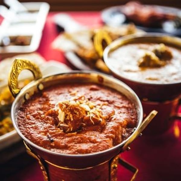 Close-up of Indian butter chicken in a copper bowl, with another curry bowl in the background.