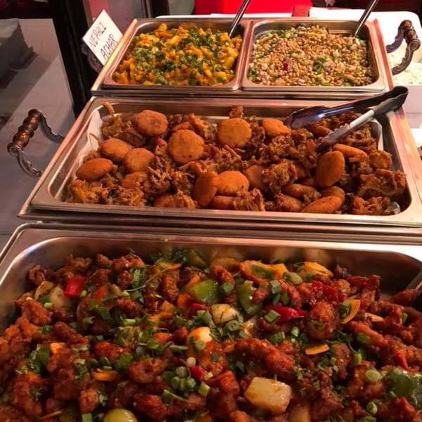 Three buffet trays of Indian food, including Nepali Achar, fried snacks, and a chili chicken dish.