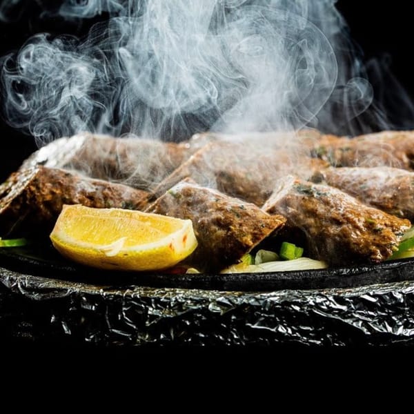 Steaming Indian seekh kebabs with a lemon wedge, served on a hot platter.