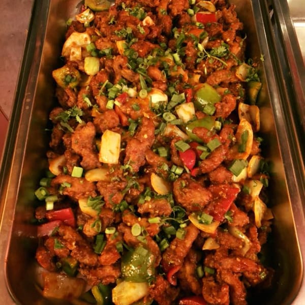 Curry Mantra's chili chicken, a popular Indian dish, with peppers, onions, and green garnish in a serving tray.