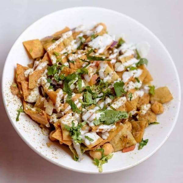 A white bowl filled with Indian chaat, featuring crispy flatbread, yogurt, and fresh cilantro.