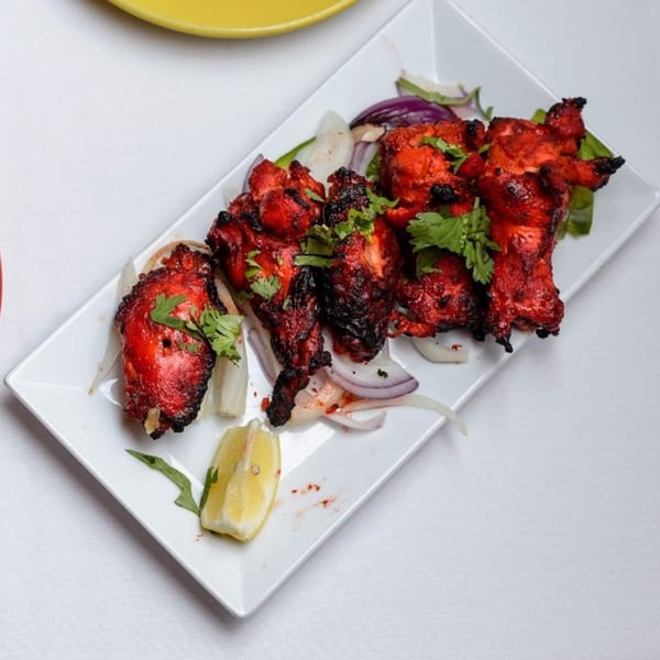 Curry Mantra's vibrant red tandoori chicken pieces, garnished with cilantro, onions, and a lemon wedge.