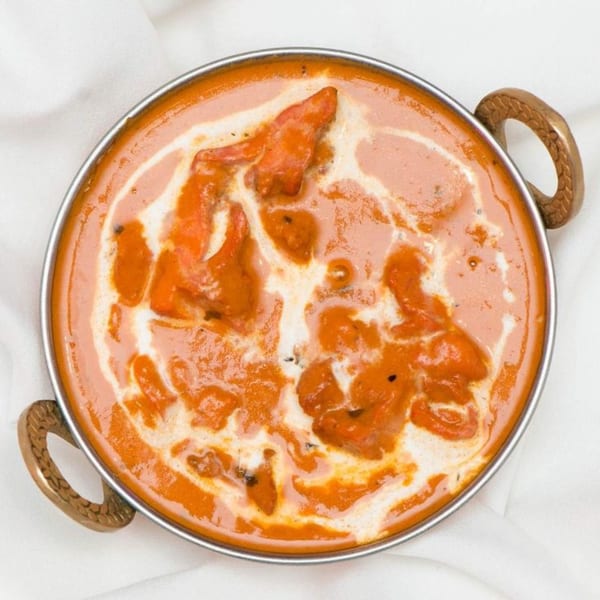 Overhead view of Curry Mantra's butter chicken, a creamy orange curry with chicken pieces in a metal bowl.