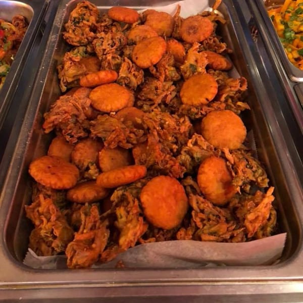 A metal tray filled with golden-brown Indian pakoras and round fried snacks at Curry Mantra.